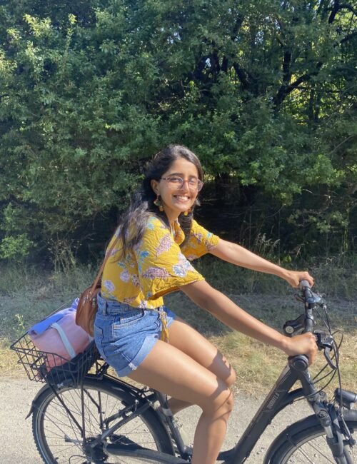 A Girl who is dressed in bright yellow teeshirt and denim shorts is cycling
