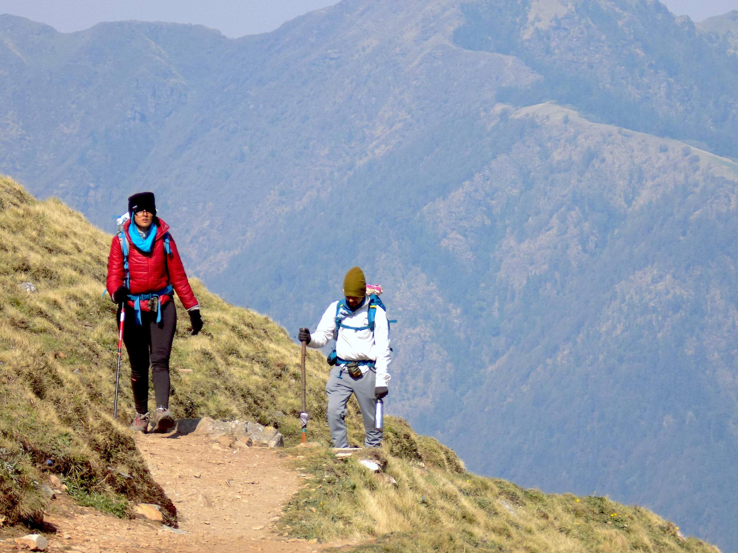 A couple trekking on the meadows each with a backpack and a walking stick