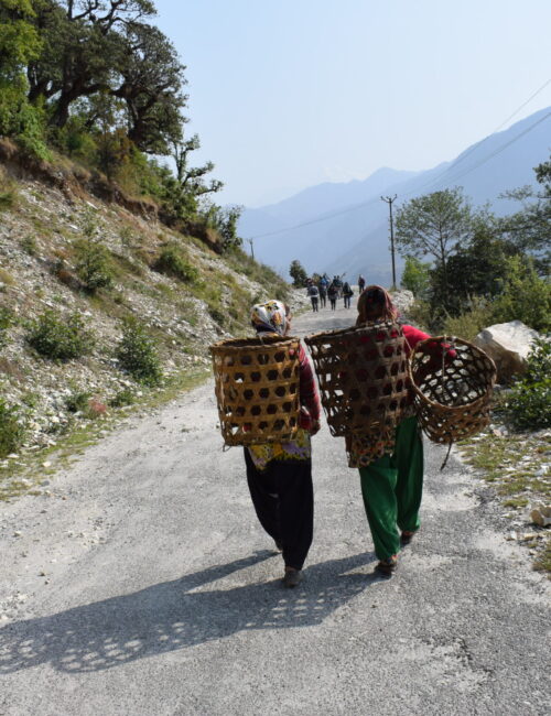 Picture of two women walking on the mountain roads with huge baskets on their back