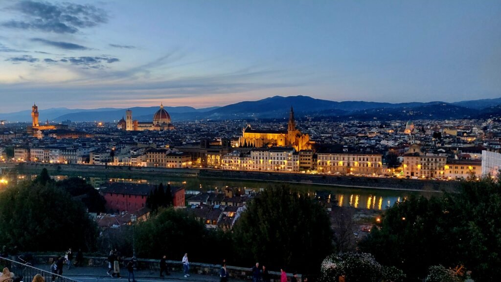Twilight panorama of Florence, Italy, with the glowing Duomo, Arno River, historic cityscape, distant hills, and a serene evening atmosphere.